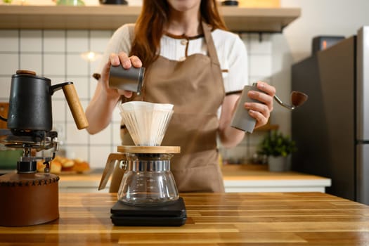 Close up of hand pouring ground coffee into a paper filter in a glass dripper over a scale.