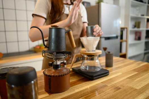 A gooseneck kettle, manual grinder, and glass dripper on wooden countertop.