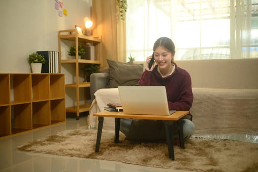 Young female freelancer working on laptop and speaking on her smartphone.