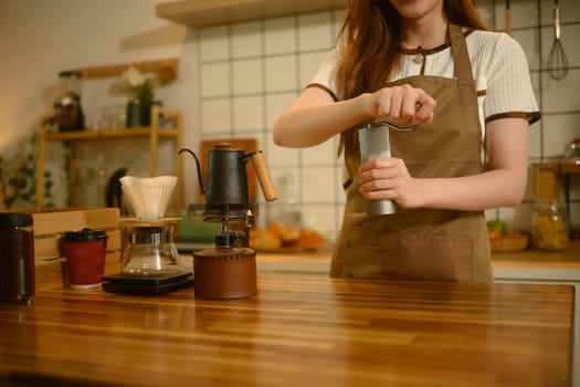 Close up shot of grinding fresh coffee beans with hand grinder at kitchen counter.