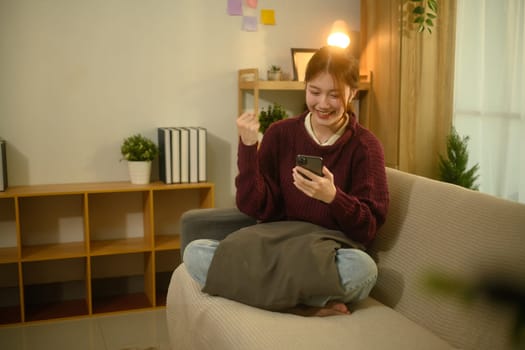 Cheerful woman raising her fist in excitement while looking at her smartphone.