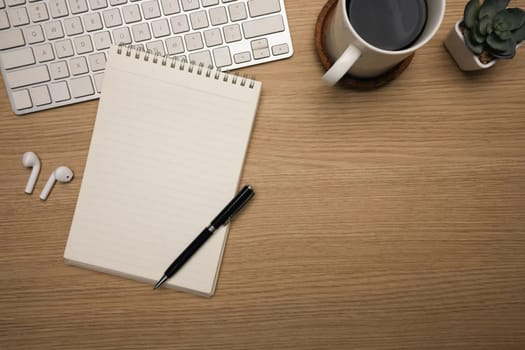 Minimalist workspace with notebook and coffee cup and wireless earbuds on wooden desk.
