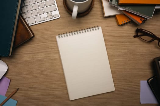 Top view of creative workspace with blank notebook surrounded by office supplies.
