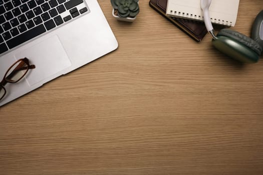 Top view shot of laptop, eyeglasses, notebook and headphones on a wooden desk.
