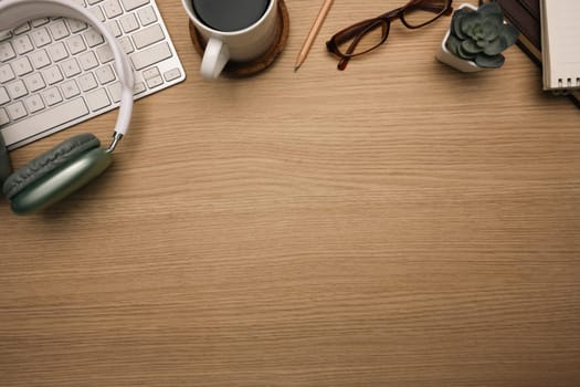 Top view shot of wooden desk with headphone, keyboard, a cup of coffee and eyeglasses.