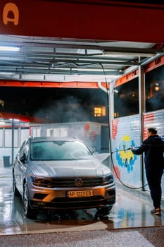 Driver at the car wash washes the hood of the car with a hose. Back view. High quality photo