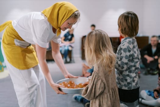 Smiling actress distributes buns to children in kindergarten from a tray in her hands. High quality photo