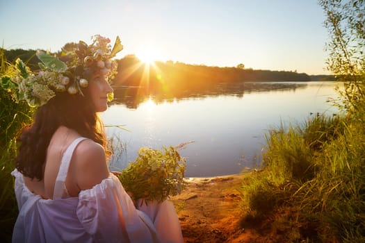 Slavic plump chubby girl in long white dress on the feast of Ivan Kupala with flowers and water in a river or lake on summer evening