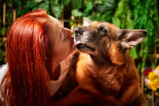 A woman shares a loving moment with her German Shepherd dog inside a warm room filled with greenery.