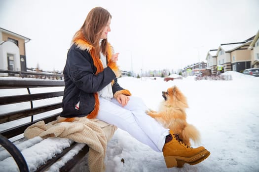 Girl interacts with her fluffy Pomeranian during a snowy day in a charming residential area.