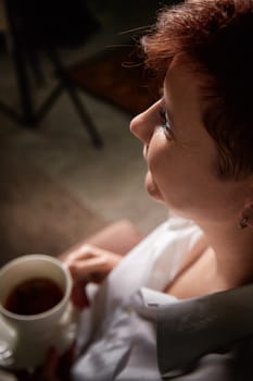 A middle-aged woman with blonde hair relaxes while holding a cup of coffee in a warm and inviting room.