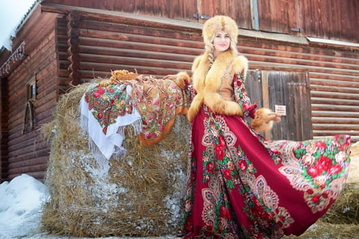Celebrating Maslenitsa, a lovely Russian girl in vibrant national attire poses gracefully with a horse in winter.