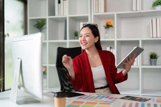 The designer smiles and raises her tablet in excitement, showcasing her joy for the creative breakthrough while brainstorming ideas.