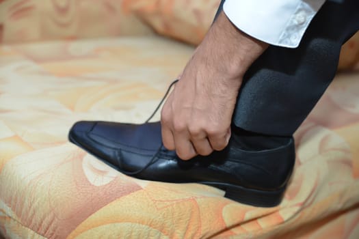 A well-dressed gentleman ties his sleek black shoes, adding the finishing touch to his elegant ensemble before stepping out in style.