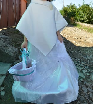 A child in a white dress carries a petal-filled basket down a rustic path, symbolizing the start of a joyous occasion