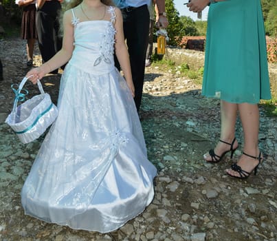 A child in a white dress carries a petal-filled basket down a rustic path, symbolizing the start of a joyous occasion