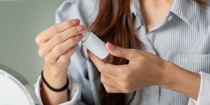 A young woman carefully holds a skincare bottle, preparing for application to enhance her beauty regimen and improve her skin health.