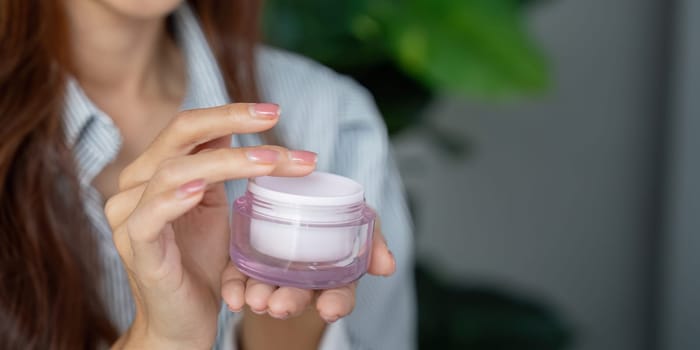This woman delicately holds a moisturizing cream jar, preparing to enrich her skincare routine. The image conveys a sense of commitment to self-care and beauty.