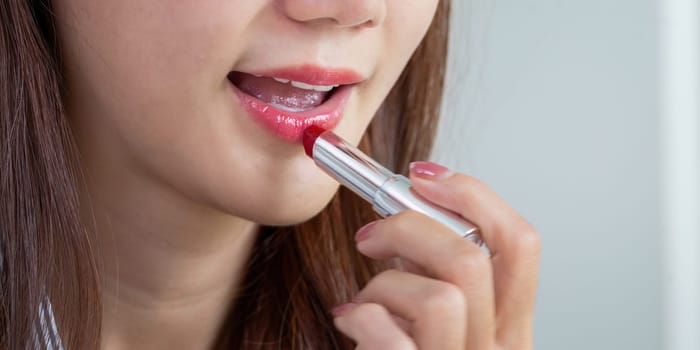 A woman carefully applies lipstick, adding shine and color to her lips as part of her daily beauty regimen.