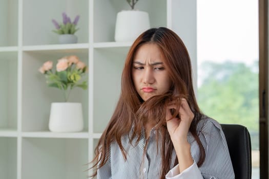 A woman looking frustrated as she examines her split ends, highlighting the importance of hair health and care in her beauty routine.