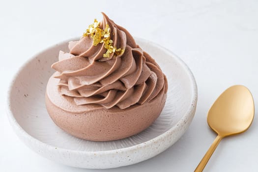 A rich chocolate mousse sits elegantly in a white ceramic bowl, adorned with delicate gold flakes, inviting a sweet and luxurious indulgence, perfect for dessert lovers.