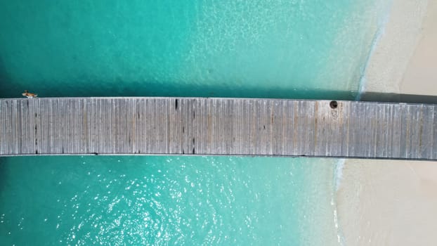 Aerial view of a wooden pier extending into crystal-clear turquoise water, creating a picturesque scene of tranquility and escape in a tropical paradise