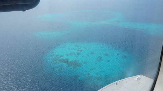 Aerial view of crystal-clear turquoise waters surrounding the coral reefs of the maldives, seen from an airplane window, showcasing the beauty of this tropical paradise
