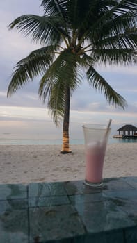 Sipping a pink cocktail on a table, surrounded by a tranquil beach and swaying palm trees, creates an atmosphere of peaceful relaxation during a beautiful dusk