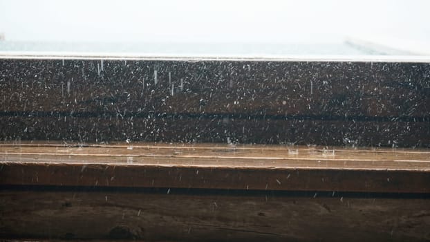 Close-up of a wooden window frame with rain and snow falling heavily against the glass during a winter storm, creating a cozy and dramatic atmosphere