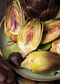 Plate full of cut purple raw romanesco artichokes on dark rustic table closeup. Fresh vegetables bought on farmers market. Cleaning and preparing to cook. Italian cousine ingredient