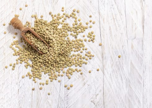 Wooden scoop full of dried green lentils on white table top view, copy space. Healthy vegetarian food, legumes plant-based protein source. Traditional mediterranean raw uncooked cousin ingredient
