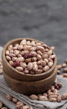 Wooden bowl full of dried pinto beans on napkin on gray table close up, copy space. Healthy vegetarian food, legumes protein source. Traditional Latin American cousin ingredient