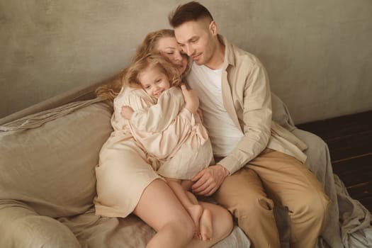 A mother, father, and young daughter embrace affectionately on a comfortable couch, enjoying a tender moment in their softly lit living room while dressed in relaxed clothing.