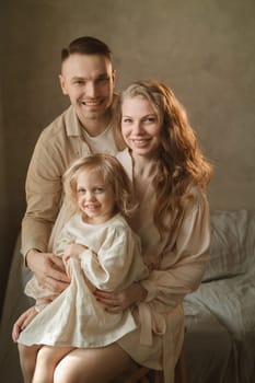 A happy family poses together in a warm and inviting indoor space, filled with soft light. The parents embrace their smiling child, showcasing love and togetherness in the moment.