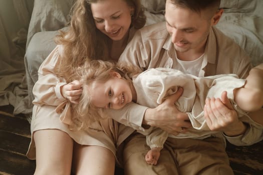 A family shares a joyful moment in a cozy room, with a child playfully lifted by a parent while the other parent watches, creating a warm atmosphere filled with laughter and love.