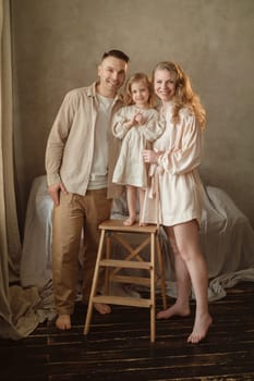 A joyful family stands together in their home, with a proud father and mother supporting their young daughter on a stool. Soft lighting enhances the warmth of the moment.