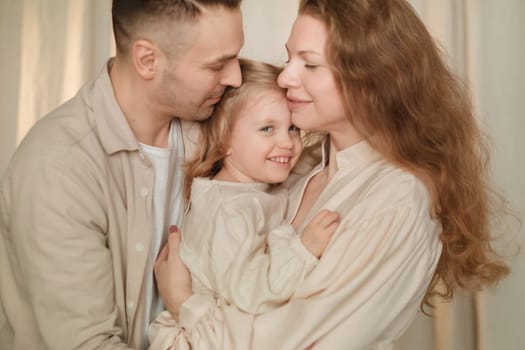 Parents share a tender moment with their smiling child in a soft-lit living room. The atmosphere is filled with warmth and love as they enjoy each other's company.