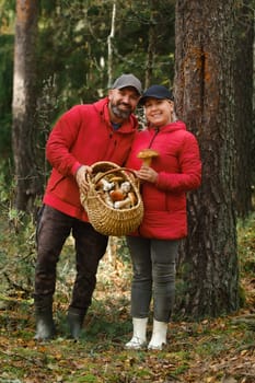 In the heart of a vibrant autumn forest, a cheerful couple poses with a basket full of freshly foraged mushrooms. They wear warm jackets and smile as they celebrate their harvest adventure.