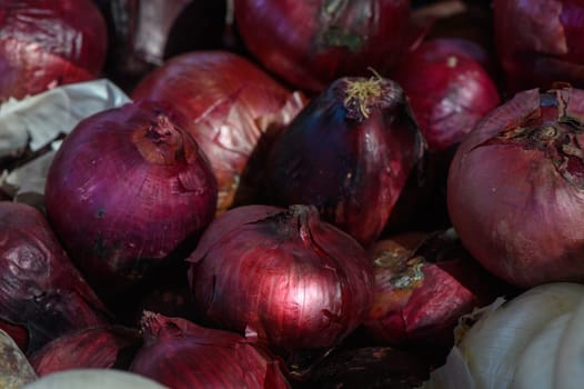 A variety of fresh red onions piled together at a lively market, basking in the afternoon sunlight. The vibrant colors and textures invite shoppers to explore the local produce offerings.