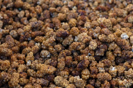 Freshly harvested mulberries shine brightly under warm sunlight, attracting shoppers at a bustling summer market.