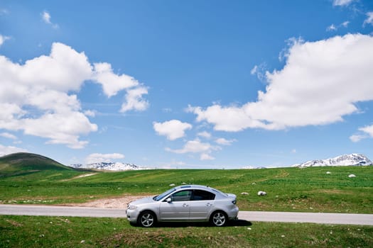 Car is standing by the side of the road on a green meadow against the backdrop of snowy mountains. High quality photo
