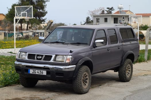 Gaziveren Cyprus -17.03.2025 A rugged Nissan Patrul pickup truck parked on a gravel road, surrounded by vibrant wildflowers. Nearby, residential homes stand under a clear blue sky, creating a tranquil atmosphere perfect for exploration.