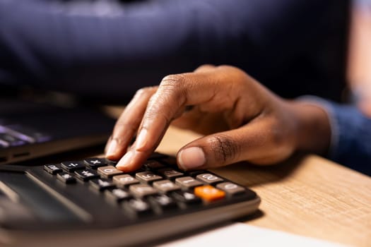 African american young couple review their expenses and taxes reports in their apartment, using a calculator and laptop to ensure accurate money management for the tax season. Close up.