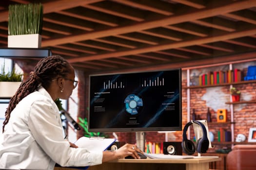 Teleworker in home office watching business presentation on PC display, looking over statistics charts. African american remote employee in apartment looking at presentation graphs on computer