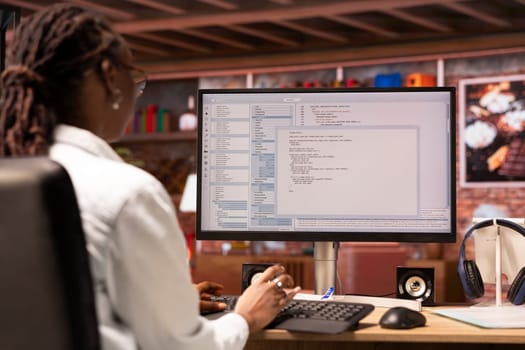 Remotely working engineer in home office looking at UI on computer monitor, typing and executing programming code. Person using coding application to write and test code in modern apartment
