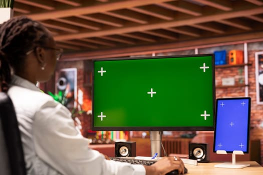 Woman browsing social media at home using green screen computer display and mockup tablet. Person talking with friends on social network online website using chroma key PC and isolated screen device