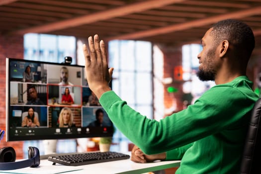 Remote worker in home office saluting colleagues during online videocall, looking at PC screen. Businessman in apartment greeting team members during videoconference meeting
