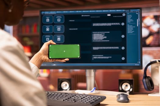 Woman using mockup smartphone to look at video tutorials on AI chatbots in home office. Person holding green screen phone to look at visual guides on artificial intelligence LLMs