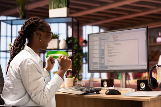 Happy programmer in home office celebrating after successfully executing programming code, looking at UI on computer monitor. Joyous IT worker satisfied after testing code and seeing good results