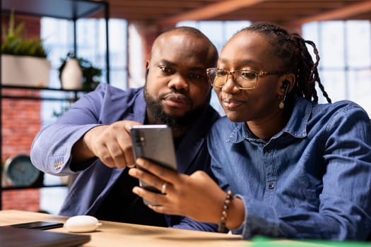 Home office users attending an online virtual call from their home, using smartphone app to participate with colleagues at a workshop. African american remote workers together at desk.